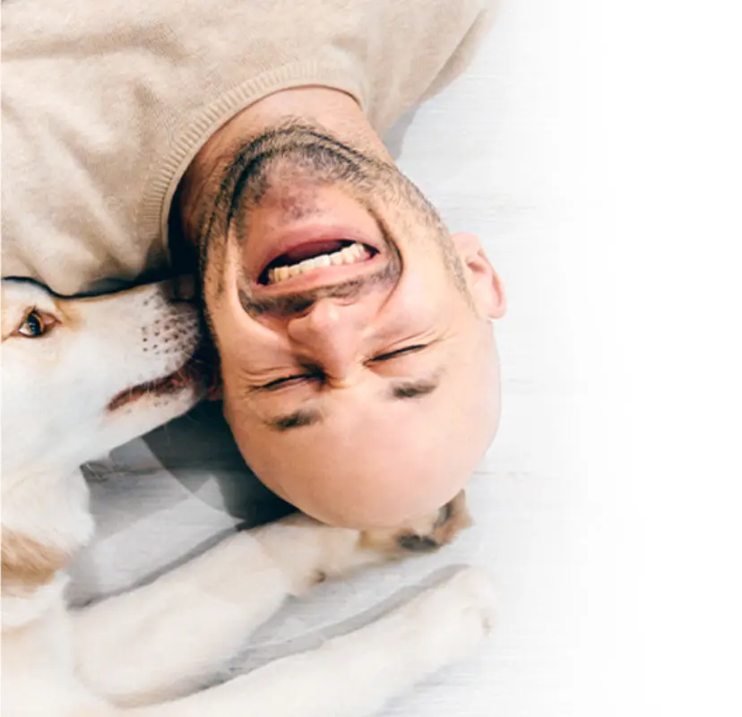 man laughing while a dog licks his ear